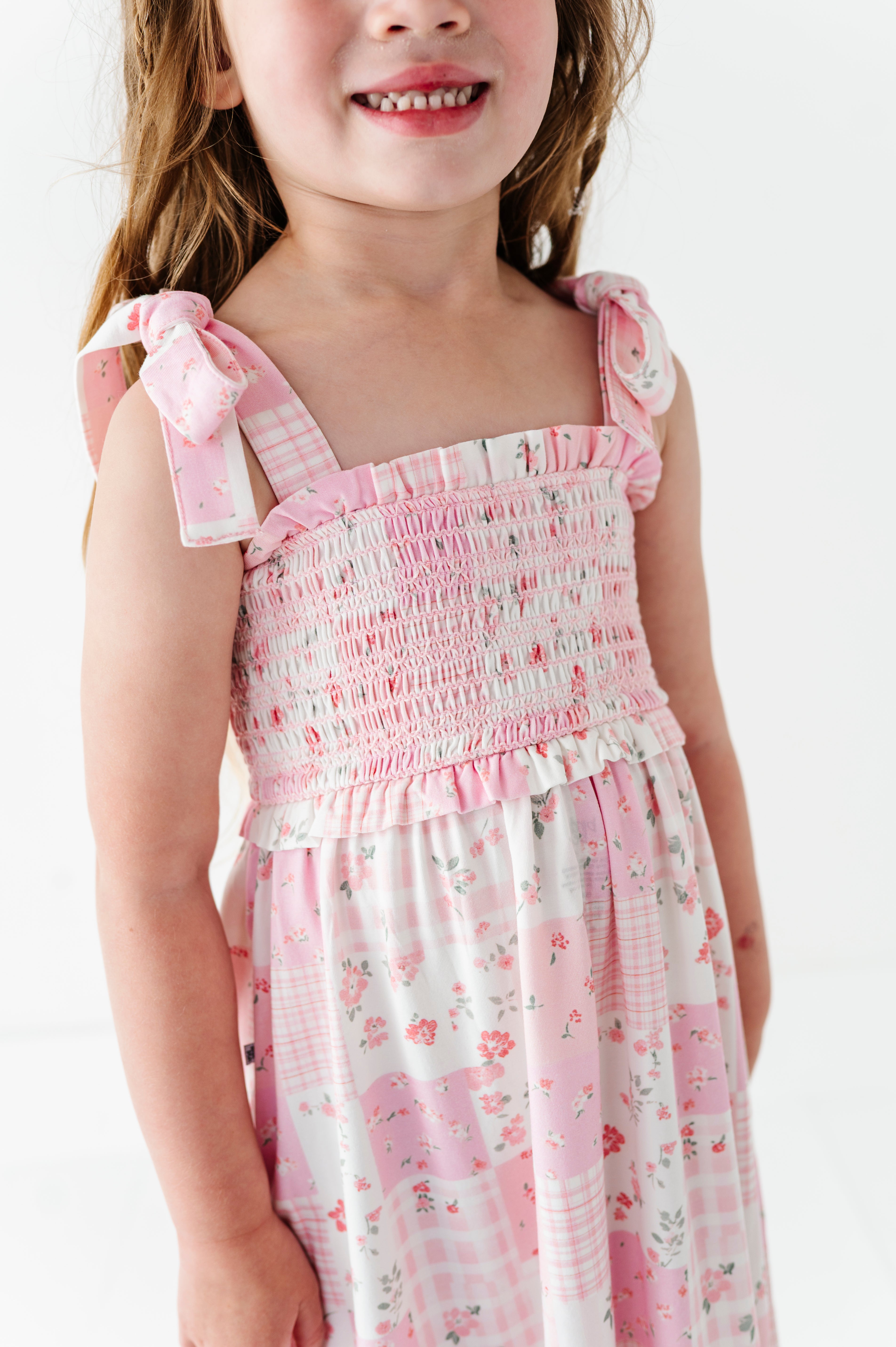 Young girl wearing a pink floral bamboo maxi dress with bow straps on a white background